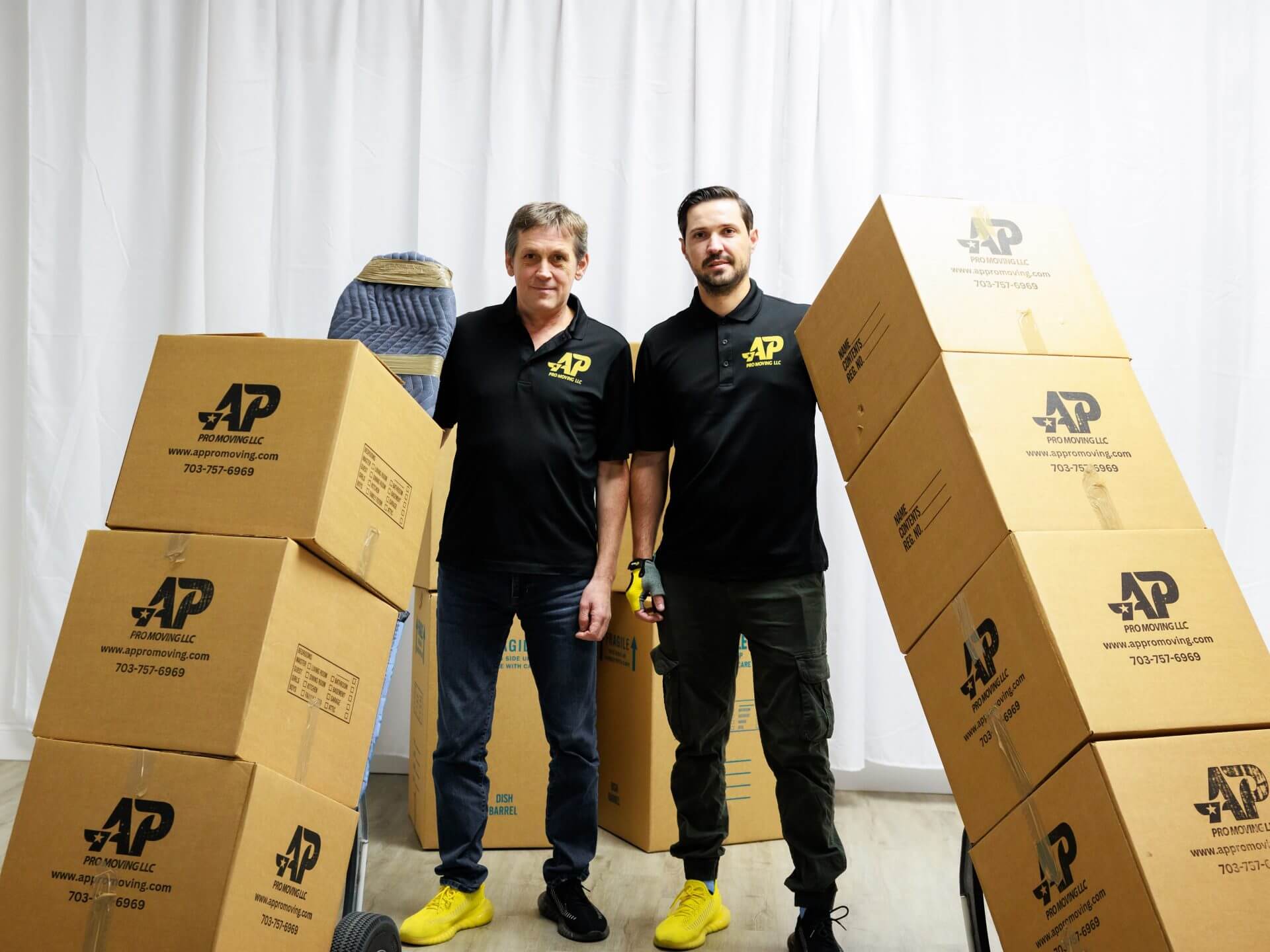two AP Pro Moving employees holding piles of cardboard moving boxes